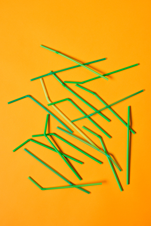 vertical conceptual flat lay shot of disposable plastic  straws lying on orange surface