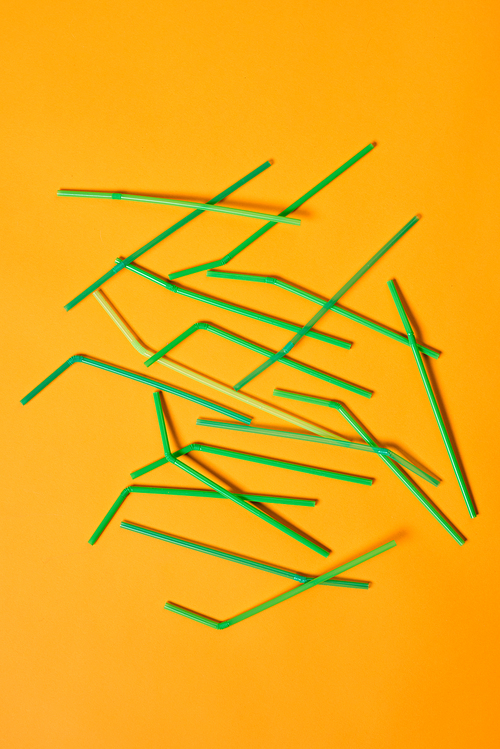 vertical conceptual flat lay image of disposable plastic  straws on bright orange background