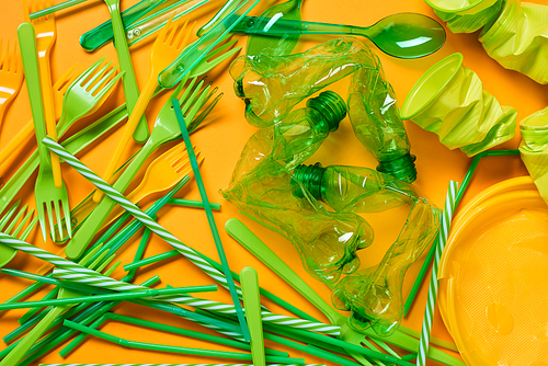 Horizontal flat lay shot of various green plastic litter lying on bright orange surface