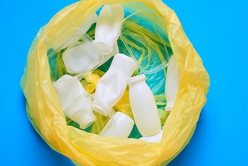Horizontal from above flat lay shot of yellow plastic garbage bag with plastic litter in it on blue background
