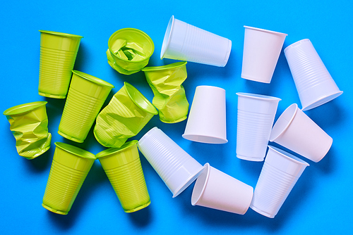 Light green anf white plastic cups on blue background, conceptual flat lay composition shot