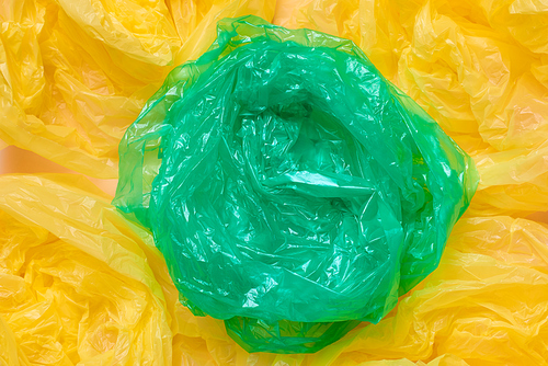 Horizontal from above flat lay shot of one empty green plastic garbage bag among yellow ones on neutral background