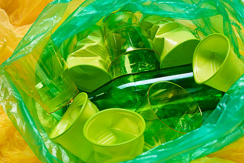 Horizontal from above shot of green plastic bin bag full of green plastic litter on yellow plastic background