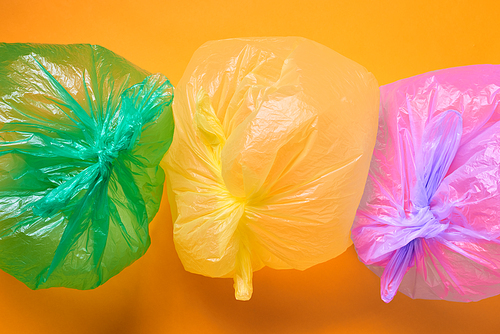 Horizontal from above conceptual shot of three multi-coloured plastic bags full of air on orange background
