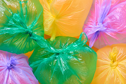 Green, yellow and violet plastic garbage bags full of air on orange background, horizontal flat lay conceptual shot