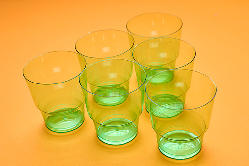 Horizontal high angle shot of six clean transparent green plastic cups on orange surface