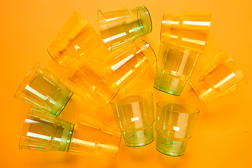 Horizontal from above flat lay shot of transparent green and yellow plastic cups lying on orange surface