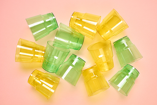 Horizontal from above flat lay shot of transparent green and yellow plastic cups lying on neutral surface