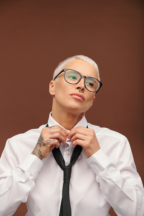 Young female with short dyed blond hair, piercing in nose and tattoos doing buttons on collar of white shirt in front of camera