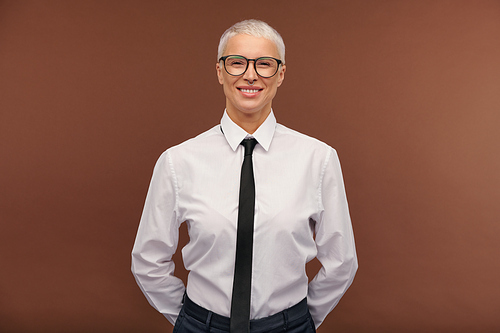 Cheerful manlike blond female in formalwear and eyeglasses looking at you with toothy smile while standing in front of camera in isolation