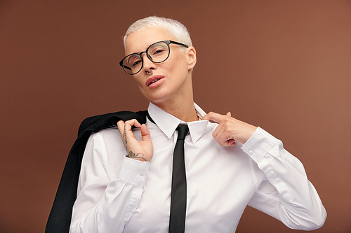 Young tired blond businesswoman in formalwear and eyeglasses loosing collar of white shirt and holding black jacket by right shoulder