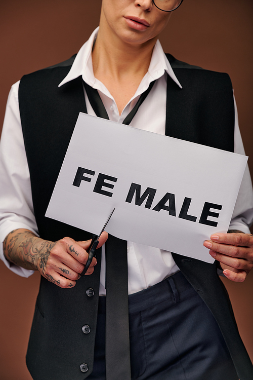 Midsection of young woman in elegant suit cutting syllable fe from word female on paper so that it became male while standing in isolation