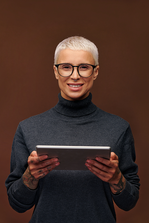 Young smiling blond businesswoman in smart casualwear and eyeglasses holding touchpad while standing in front of camera in isolation