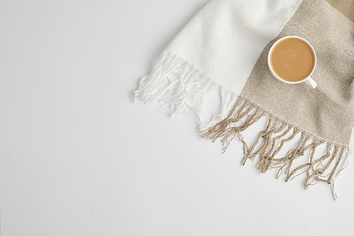 Flat lay of small white porcelain cup of fresh aromatic cappuccino on checkered linen or cotton scarf with copyspace on the left