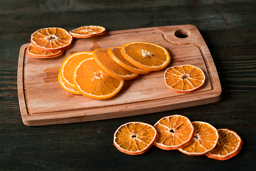 Heap of slices of fresh and dry oranges on rectangular wooden chopping board on dark table that can be used as background
