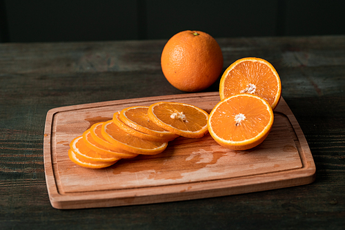 Group of fresh orange slices and halves of the fruits on wooden chopping board on the kitchen table cut by housewife for eating