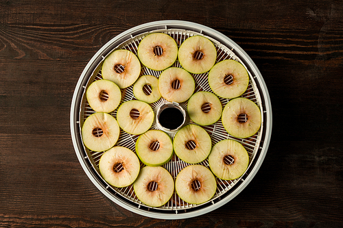 Flat layout of circle plastic tray of fruit dryer with slices of fresh apples over brown wooden table that can be used as background
