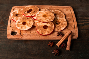 Ripe red apple, two sticks of cinnamon, star anise and wooden chopping board with slices of fresh fruit sprinkled with ground spices