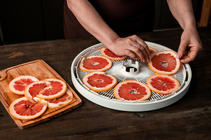 Hands of housewife with smartphone over round tray of fruit dryer with fresh sliced grapefruit on table while making photo of them