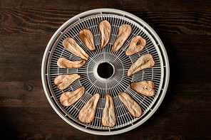 Top down view of dried pear slices on round tray of fruit dryer in the center of dark wooden kitchen table with copyspace around