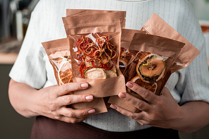 Several paper packages with homemade dried fruits in hands of contemporary housewife holding them by her chest