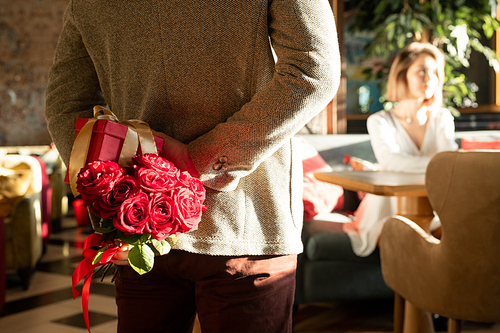 Unrecognizable man appearing on date in restaurant with roses and gift box for his girlfriend, horizontal shot
