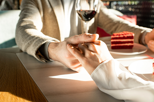 Unrecognizable man and woman in love spending time in modern restaurant gently holding hands, horizontal shot