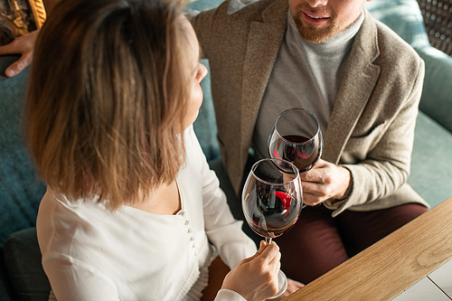 High angle horizontal shot of man and woman in love clinking glasses with red wine while spending time in restaurant