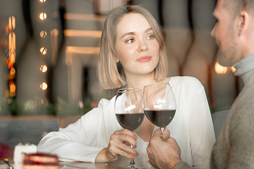 Horizontal portrait of attractive Caucasian woman and man sitting in restaurant clinking glasses with red wine