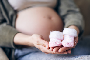 Close-up of unrecognizable pregnant woman holding small pink socks for baby