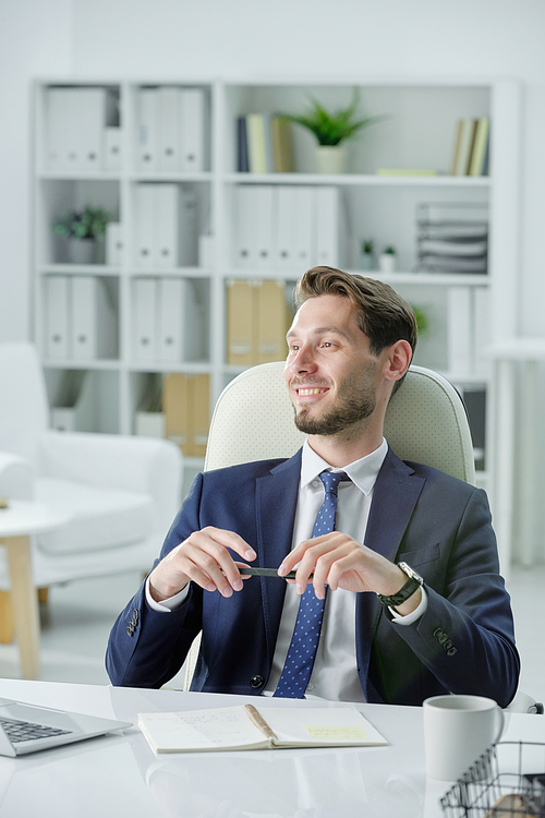 Smiling handsome businessman with stubble sitting at desk and listening to business partner while meeting with him in office