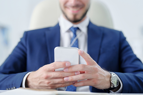 Close-up of businessman in suit using smartphone while texting message to colleague