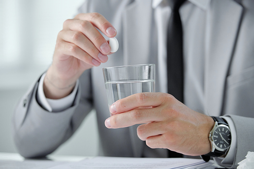 Close-up of unrecognizable businessman in wristwatch dissolving pill into water while suffering from morning hangover at workplace