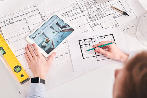 Above view of architect using digital tablet and blueprints while working on floor plan of flat