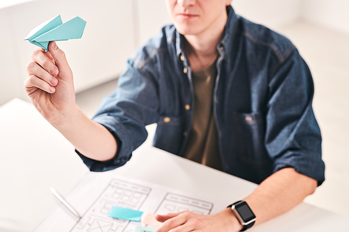 Close-up of young man sitting at table and throwing paper plane while working on UI design in office