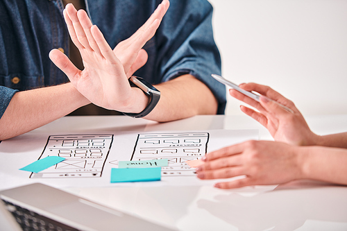 Close-up of unrecognizable user interface designer showing ban sign while disagreeing with colleague at meeting