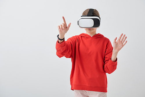 Contemporary teenage girl in red hoodie and vr headset pointing at virtual display while preparing or making presentation