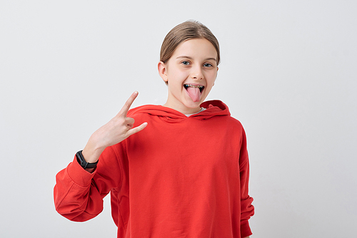 Portrait of crazy cool teenage girl in braces showing horn gesture and sticking tongue out against white background