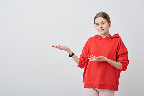 Portrait of teenage girl in red hoodie gesturing aside while presenting her idea