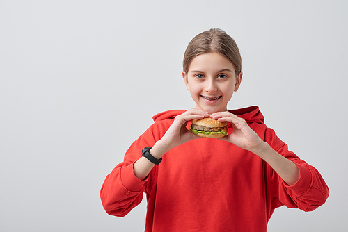 Portrait of smiling teenager in red sweatshirt eating burger against white background