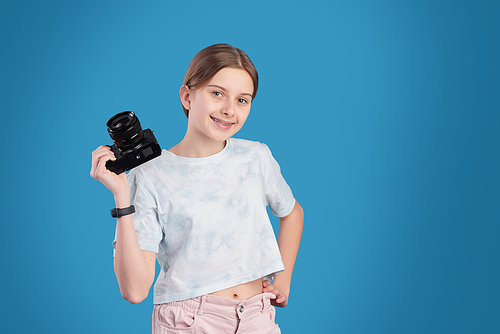 Portrait of smiling pretty teenage girl posing with professional camera against blue background