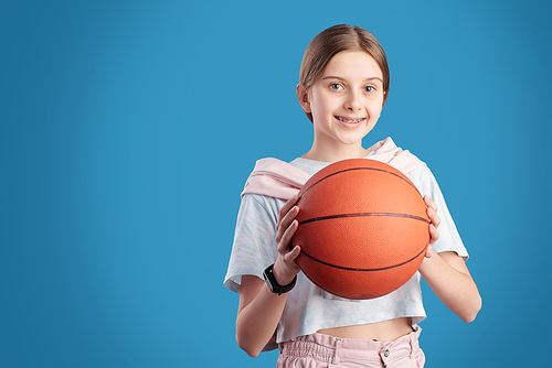 Portrait of smiling teenage girl holding basketball against blue background