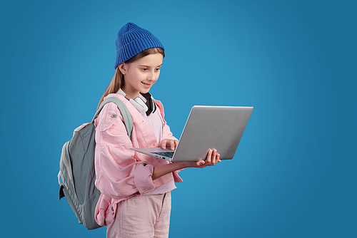 Content modern teenage girl with satchel surfing internet on laptop against blue background