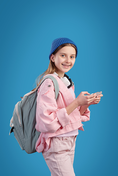 Casual clever teenage girl with backpack and mobile gadget scrolling in smartphone while going to school or college