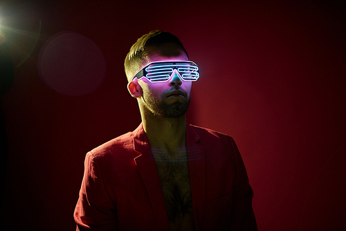 Bearded young man in jacket wearing special futuristic new generated eyewear standing over dark background in isolation
