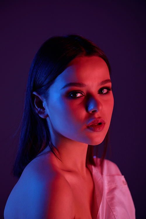 Portrait of beautiful brunette girl with naked shoulder against dark background, neon color effect