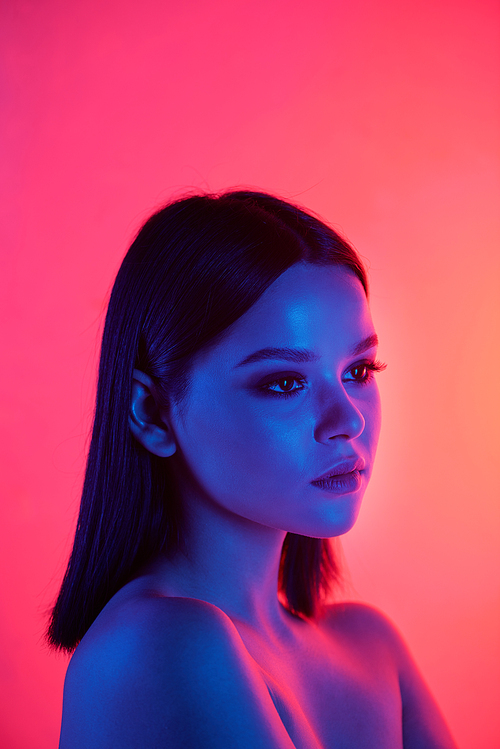 Serious pretty brunette woman with naked shoulders looking away against neon pink background