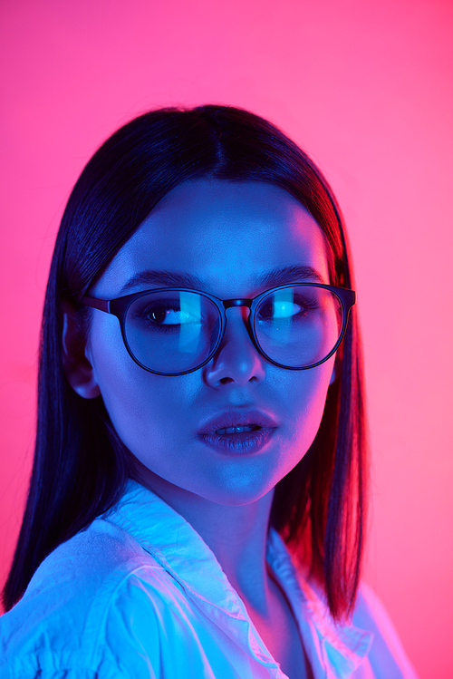 Young woman with dark long hair and perfect makeup wearing stylish eyeglasses and white shirt on pink background