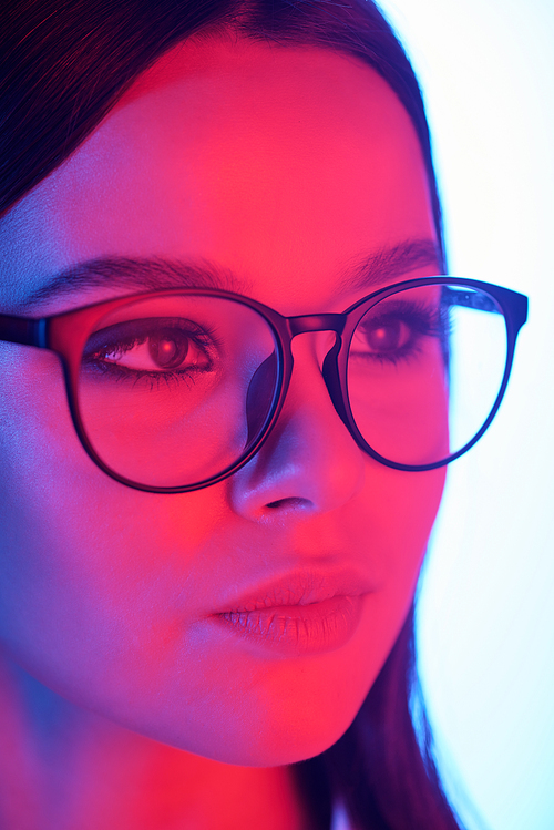 Young beautiful brunette woman with pink neon backlit face wearing eyeglasses in front of camera in isolation