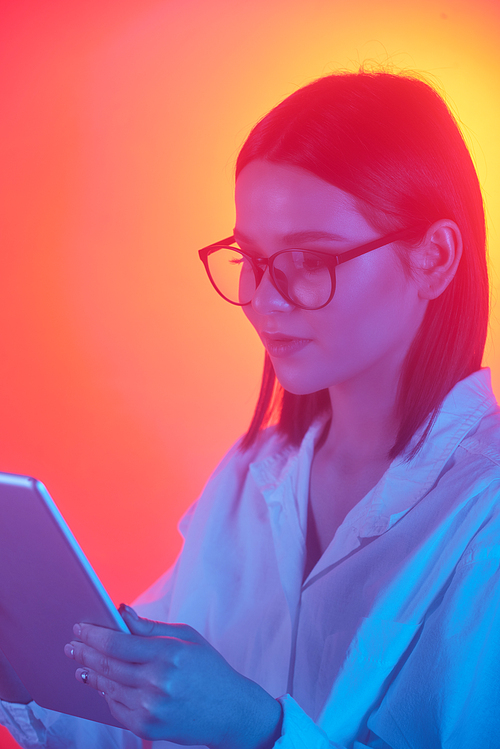 Content smart young woman in eyewear using digital tablet in bright yellow light